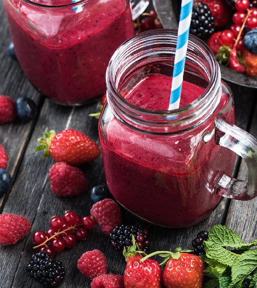 Glaskrug mit Griff gefüllt mit rotem Smoothie, umgeben von frischen Beeren auf Holzoberfläche