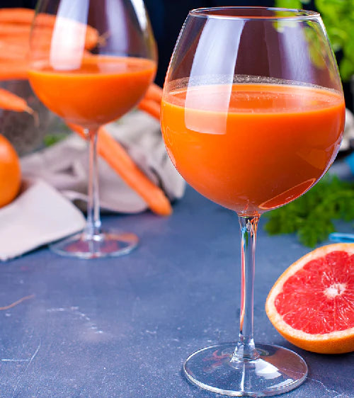 Zwei Gläser Karottensaft mit Karotten und einer Grapefruit auf blauer Oberfläche
