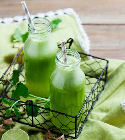 Zwei grüne Smoothies in Glaskrügen mit Strohhalmen auf grünem Stoff