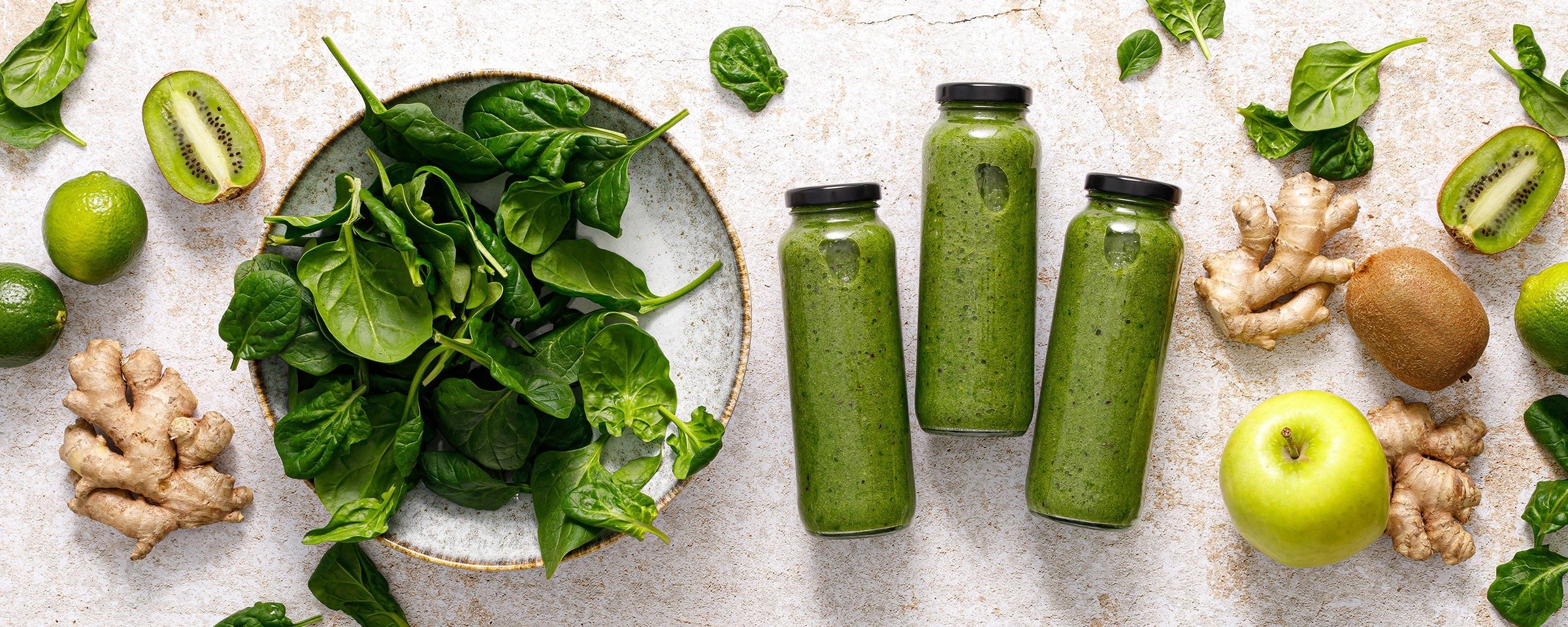 Zelené lahve na smoothie Kuvings s kiwi, špenátem a zázvorem, zdůrazňující čerstvé ingredience pro zdravé domácí šťávy a smoothies.