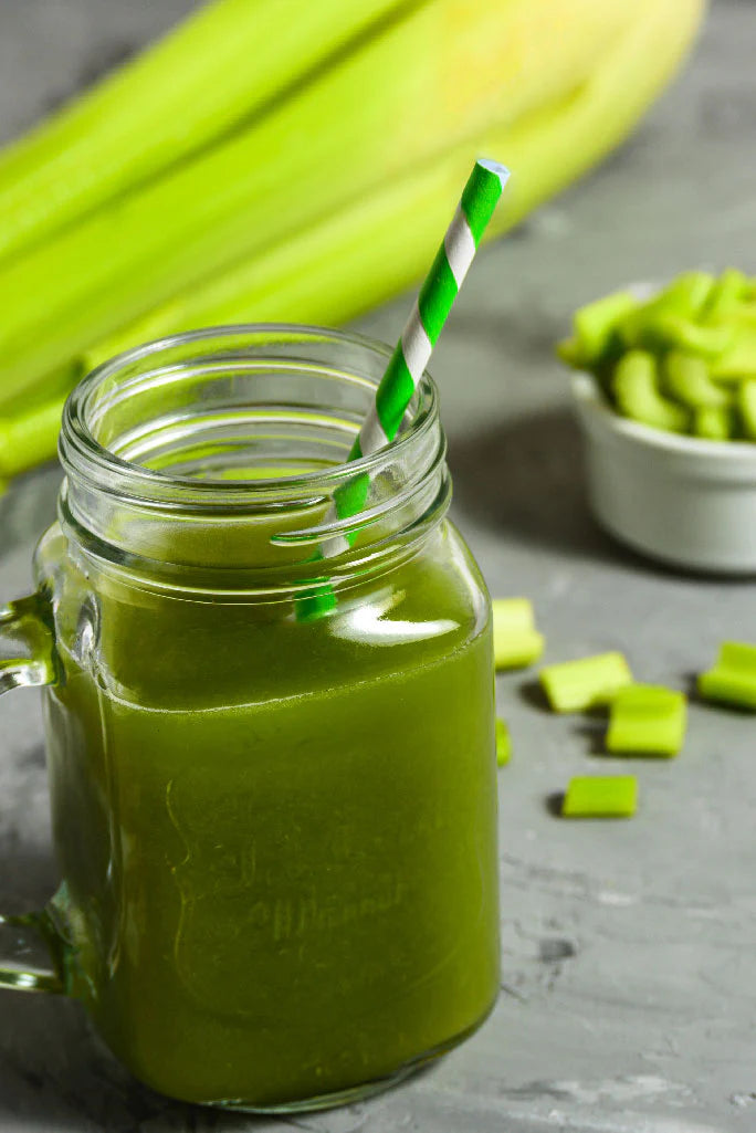 Grüner Smoothie in einem Einmachglas mit Selleriestangen und grünem Gemüse im Hintergrund