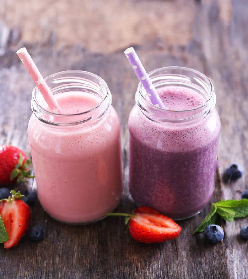 Zwei Smoothies in Glaskrügen mit Strohhalmen auf Holzoberfläche, umgeben von Beeren