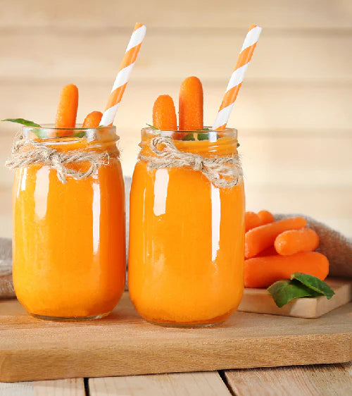 Zwei Krüge Karottensaft mit Strohhalmen und Karotten auf Holzoberfläche