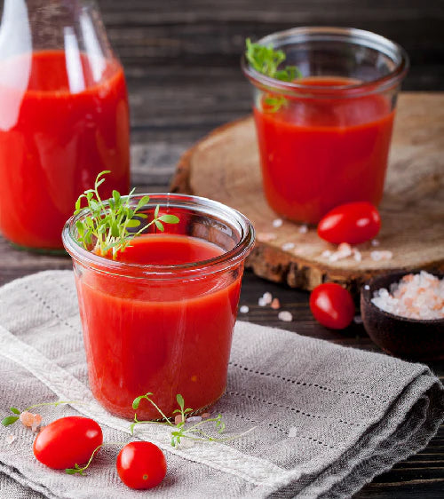 Tomatensaft in Glaskrügen mit Kirschtomaten auf Holzoberfläche